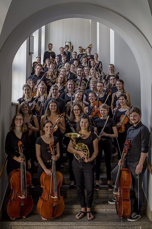 Das Orchester der HTWK Leipzig (Foto: R. Weinhold) Auf einer Treppe stehen alle Mitglieder des Orchesters. Vorne die Streicher wie Celli und Geigen, hinten die Bläser wie Hörner und Trompeten.
